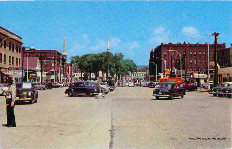 Main Street, Keene, New Hampshire. Note the police officer at left directing traffic. To the right of the orange truck is the Keene Diner. Postcard, photo